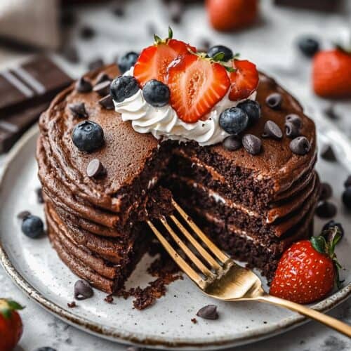 Sliced chocolate protein pancakes topped with berries, whipped cream, and chocolate chips.