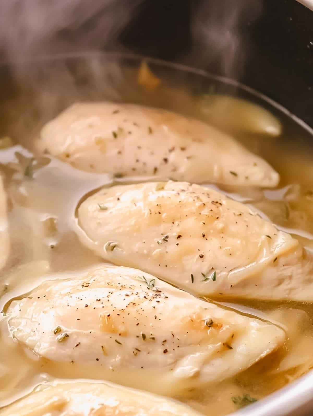 Chicken breasts simmering in a pot of seasoned broth.