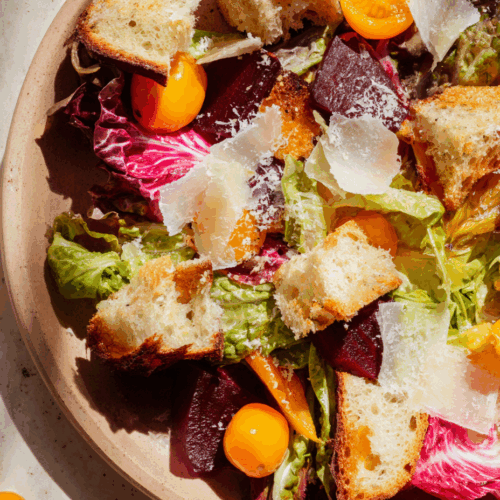 Spring salad with garlic confit beets, halved kumquats, torn butter lettuce, pink radicchio, Tomme cheese, and focaccia croutons on a stone plate