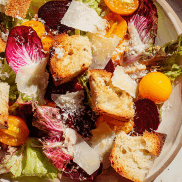 Spring salad with garlic confit beets, halved kumquats, torn butter lettuce, pink radicchio, Tomme cheese, and focaccia croutons on a stone plate